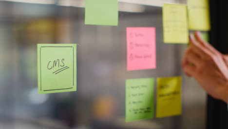Close-Up-Of-Woman-Putting-Sticky-Note-With-CMS-Written-On-It-Onto-Transparent-Screen-In-Office-2