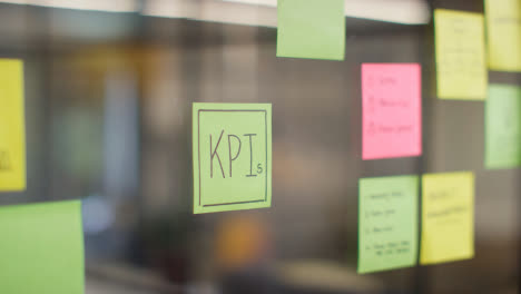 Close-Up-Of-Woman-Putting-Sticky-Note-With-KPIs-Written-On-It-Onto-Transparent-Screen-In-Office-1