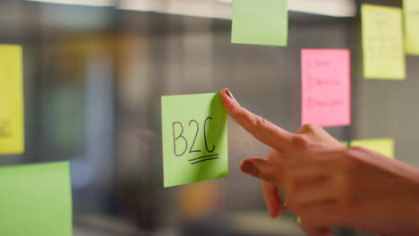 Close-Up-Of-Woman-Putting-Sticky-Note-With-B2C-Written-On-It-Onto-Transparent-Screen-In-Office-2