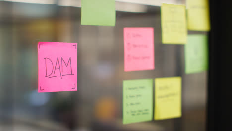 Close-Up-Of-Woman-Putting-Sticky-Note-With-DAM-Written-On-It-Onto-Transparent-Screen-In-Office-1