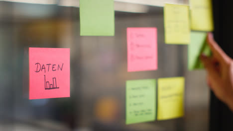 Close-Up-Of-Woman-Putting-Sticky-Note-With-German-Word-Daten-Or-Data-Written-On-It-Onto-Transparent-Screen-In-Office-2