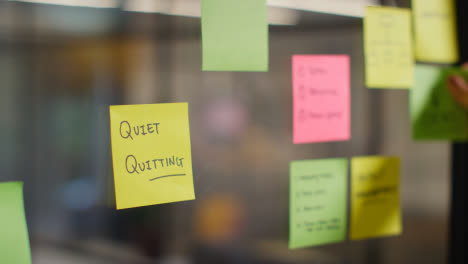 Close-Up-Of-Woman-Putting-Sticky-Note-With-Quiet-Quitting-Written-On-It-Onto-Transparent-Screen-In-Office-1