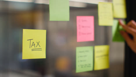Close-Up-Of-Woman-Putting-Sticky-Note-With-Tax-Written-On-It-Onto-Transparent-Screen-In-Office-2