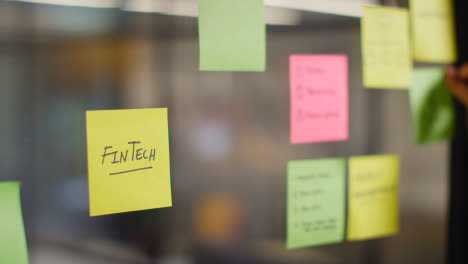 Close-Up-Of-Woman-Putting-Sticky-Note-With-Fintech-Written-On-It-Onto-Transparent-Screen-In-Office-2