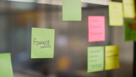 Close-Up-Of-Woman-Putting-Sticky-Note-With-Finance-Written-On-It-Onto-Transparent-Screen-In-Office-2