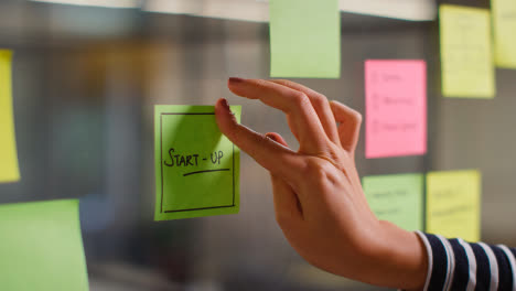 Close-Up-Of-Woman-Putting-Sticky-Note-With-Start-Up-Written-On-It-Onto-Transparent-Screen-In-Office-2