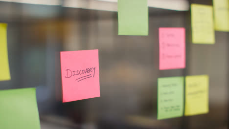 Close-Up-Of-Woman-Putting-Sticky-Note-With-Discovery-Written-On-It-Onto-Transparent-Screen-In-Office-1