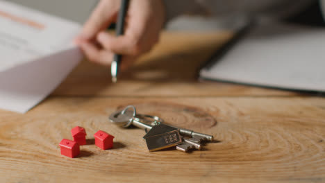Hauskaufkonzept-Mit-Schlüsseln-Am-Hausförmigen-Schlüsselring-Und-Person,-Die-Finanzen-überprüft