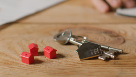 Hauskaufkonzept-Mit-Schlüsseln-Am-Hausförmigen-Schlüsselring-Und-Person,-Die-Die-Finanzen-überprüft-2