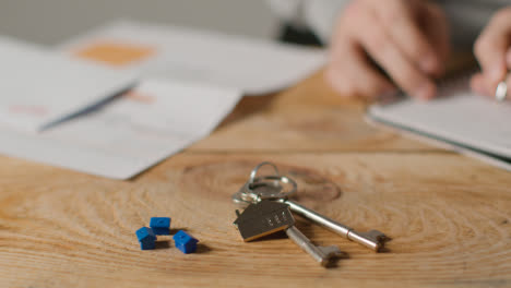 Hauskaufkonzept-Mit-Schlüsseln-Am-Hausförmigen-Schlüsselring-Und-Person,-Die-Finanzen-überprüft-5