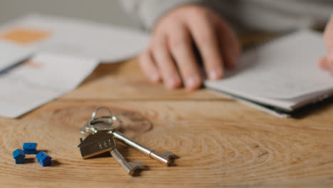 Hauskaufkonzept-Mit-Schlüsseln-Am-Hausförmigen-Schlüsselring-Und-Person,-Die-Finanzen-überprüft-6