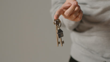 Hauskaufkonzept-Mit-Person,-Die-Schlüssel-Auf-Hausförmigem-Schlüsselring-Vor-Grauem-Hintergrund-Hält-2