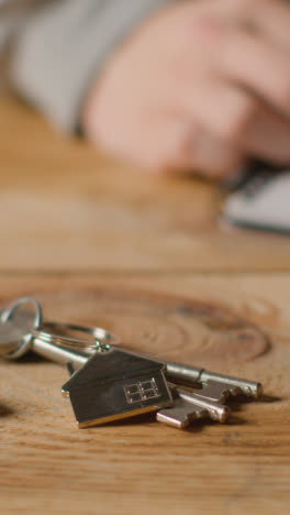 Vertical-Video-Home-Buying-Concept-With-Keys-On-House-Shaped-Keyring-And-Person-Checking-Finances