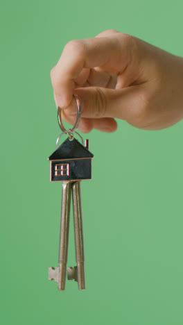 Vertical-Video-Home-Buying-Concept-With-Person-Holding-Keys-On-House-Shaped-Keyring-Against-Green-Screen-Background