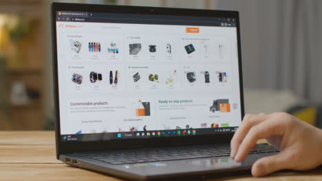 Person-Zu-Hause,-Die-Online-Einkauft-Und-Sich-Die-Alibaba-website-Auf-Einem-Laptop-Ansieht