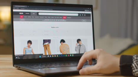 Person-At-Home-Shopping-Online-Looking-At-Asos-Website-On-Laptop