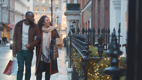 Couple-Walking-Arm-In-Arm-Through-Street-On-Christmas-Shopping-Trip-To-London-