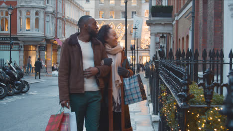 Couple-Walking-Arm-In-Arm-Through-Street-On-Christmas-Shopping-Trip-To-London-3