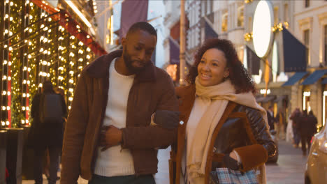 Couple-Walking-Arm-In-Arm-Through-Street-On-Christmas-Shopping-Trip-To-London-5
