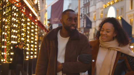 Couple-Walking-Arm-In-Arm-Through-Street-On-Christmas-Shopping-Trip-To-London-6