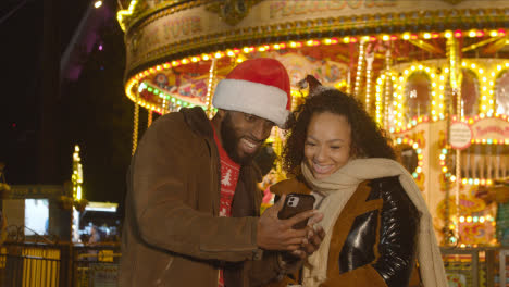 Pareja-Celebrando-La-Navidad-De-Pie-Junto-A-La-Rotonda-Del-Recinto-Ferial-En-El-Banco-Sur-De-Londres-Por-La-Noche-Con-El-Teléfono-Móvil-1