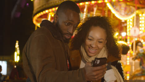 Pareja-De-Pie-Junto-A-La-Rotonda-Del-Recinto-Ferial-En-El-Banco-Sur-De-Londres-Por-La-Noche-Con-El-Teléfono-Móvil-3