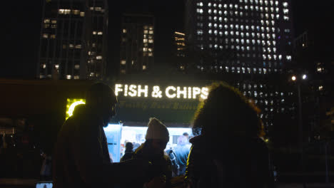 Clientes-Frente-Al-Puesto-De-Pescado-Y-Papas-Fritas-En-El-Banco-Sur-De-Londres-Por-La-Noche