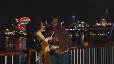 Couple-On-Date-Standing-On-London-South-Bank-At-Night-Eating-Chips-1