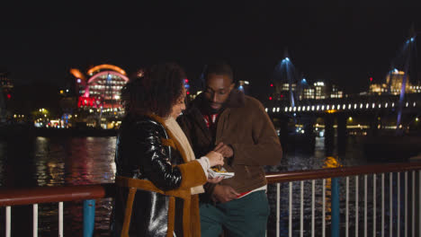 Couple-On-Date-Standing-On-London-South-Bank-At-Night-Eating-Chips-2