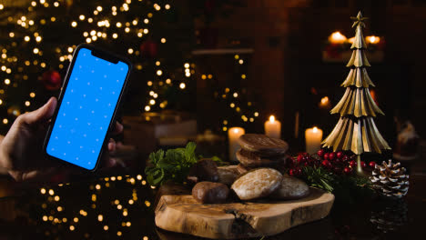 Navidad-En-Casa-Con-Lebkuchen-Navideño-Alemán-Tradicional-Y-Persona-Con-Teléfono-Móvil-De-Pantalla-Azul