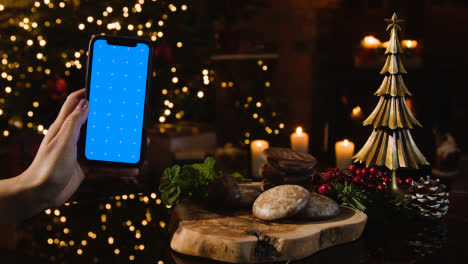 Christmas-At-Home-With-Person-Eating-Traditional-German-Christmas-Lebkuchen-And-Person-Holding-Blue-Screen-Mobile-Phone