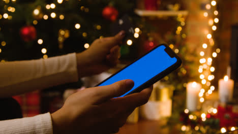 Weihnachten-Zu-Hause-Mit-Person,-Die-Kartenkauf-Auf-Handy-Mit-Blauem-Bildschirm-Tätigt
