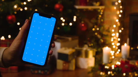 Weihnachten-Zu-Hause-Mit-Person,-Die-Handy-Mit-Blauem-Bildschirm-Hält