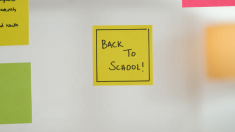 Close-Up-Of-Woman-Putting-Sticky-Note-With-Back-To-School-Written-On-It-Onto-Transparent-Screen-In-Office-