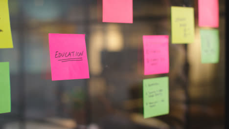 Close-Up-Of-Woman-Putting-Sticky-Note-With-Education-Written-On-It-Onto-Transparent-Screen-In-Office-1