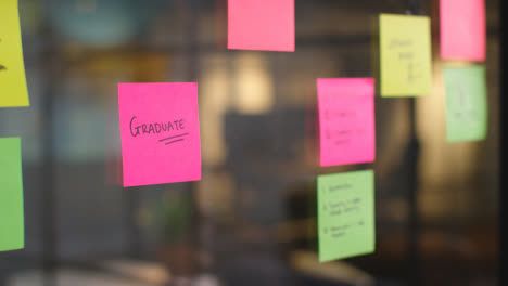 Close-Up-Of-Woman-Putting-Sticky-Note-With-Graduate-Written-On-It-Onto-Transparent-Screen-In-Office-1