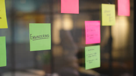 Close-Up-Of-Woman-Putting-Sticky-Note-With-Engineering-Written-On-It-Onto-Transparent-Screen-In-Office-1