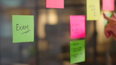 Close-Up-Of-Woman-Putting-Sticky-Note-With-Exam-Written-On-It-Onto-Transparent-Screen-In-Office-2