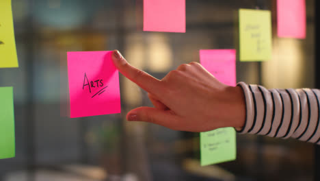 Close-Up-Of-Woman-Putting-Sticky-Note-With-Arts-Written-On-It-Onto-Transparent-Screen-In-Office-1