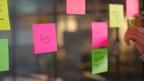 Close-Up-Of-Woman-Putting-Sticky-Note-With-Arts-Written-On-It-Onto-Transparent-Screen-In-Office-2