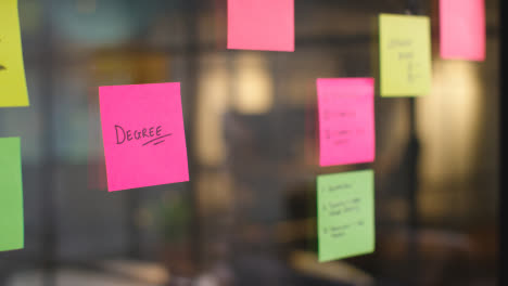 Close-Up-Of-Woman-Putting-Sticky-Note-With-Degree-Written-On-It-Onto-Transparent-Screen-In-Office-1