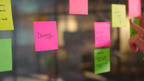 Close-Up-Of-Woman-Putting-Sticky-Note-With-Degree-Written-On-It-Onto-Transparent-Screen-In-Office-2