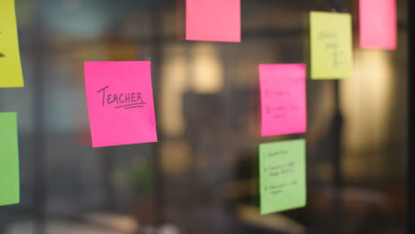 Close-Up-Of-Woman-Putting-Sticky-Note-With-Teacher-Written-On-It-Onto-Transparent-Screen-In-Office-1