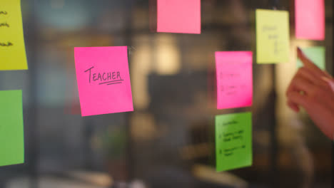 Close-Up-Of-Woman-Putting-Sticky-Note-With-Teacher-Written-On-It-Onto-Transparent-Screen-In-Office-2