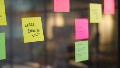 Close-Up-Of-Woman-Putting-Sticky-Note-With-Learn-English-Written-On-It-Onto-Transparent-Screen-In-Office-1