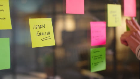 Close-Up-Of-Woman-Putting-Sticky-Note-With-Learn-English-Written-On-It-Onto-Transparent-Screen-In-Office-2