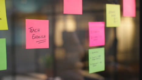 Close-Up-Of-Woman-Putting-Sticky-Note-With-Teach-English-Written-On-It-Onto-Transparent-Screen-In-Office-2