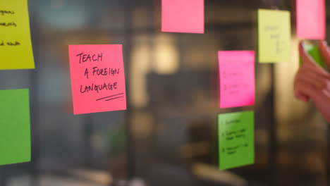 Close-Up-Of-Woman-Putting-Sticky-Note-With-Teach-A-Foreign-Language-Written-On-It-Onto-Transparent-Screen-In-Office-3