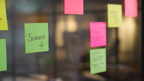 Close-Up-Of-Woman-Putting-Sticky-Note-With-Science-Written-On-It-Onto-Transparent-Screen-In-Office-1