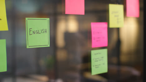 Close-Up-Of-Woman-Putting-Sticky-Note-With-English-Written-On-It-Onto-Transparent-Screen-In-Office-1